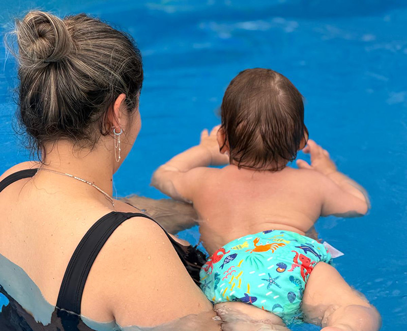 שחיית תינוקות עם מדריכה המחזיקה תינוק במים ותומכת בתנועה ראשונית