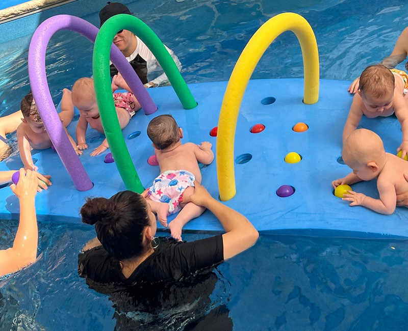 שיעור שחיית תינוקות בבריכה עם מדריכות ותינוקות על מתקן פעילות צבעוני במים