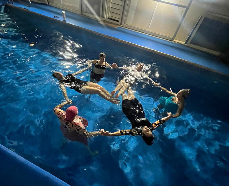 טיפול קבוצתי במים עם משתתפים צפים יחד במעגל בבריכה בליווי מדריכה