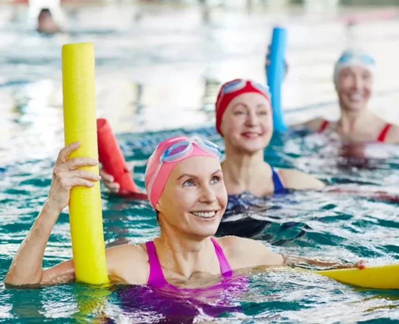 נשים מבוגרות מתאמנות באירובי מים בבריכה עם מצופי נודל באווירה חיובית