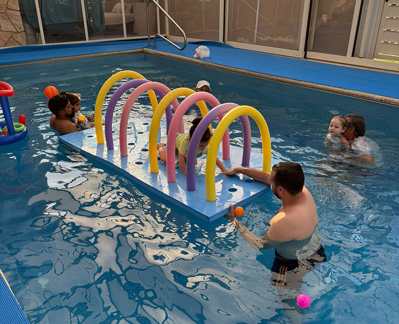 שיעור שחייה לילדים בבריכה עם מתקן משחק צבעוני וליווי מדריכים במים